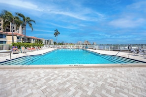 A clear blue pool with a 'NO DIVING' sign, surrounded by lounge chairs and palm trees, with a view of buildings in the background. - Relaxed Island Living Condo Golf Course Views (St.Petersburg)