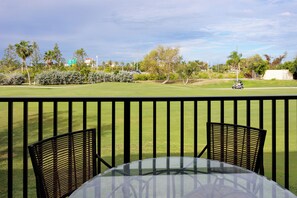 En uteplats med två stolar och ett bord, med utsikt över en välskött gräsmatta och en golfbana.