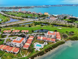 An aerial view of a coastal resort with multiple buildings, a marina, and a golf course. - Relaxed Island Living Condo Golf Course Views (St.Petersburg)