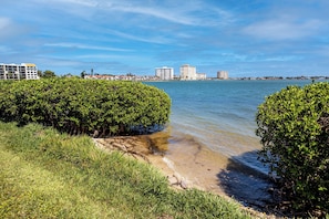 A coastal view with a clear sky, a sandy beach, and dense green shrubbery. - Relaxed Island Living Condo Golf Course Views (St.Petersburg)