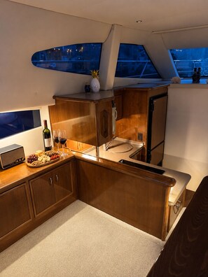 A compact kitchen with a built-in stove, a small sink, and a countertop with a radio, wine bottle, and snacks. - Waterfront Yacht Tiki Bar Food & Drinks (Clearwater)