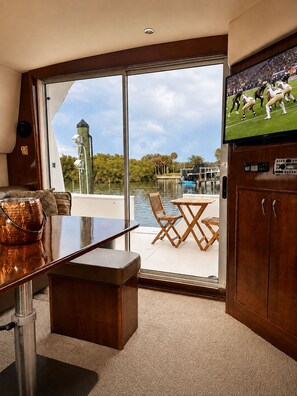 A boat interior with a dining area, a television, and a view of the water outside.