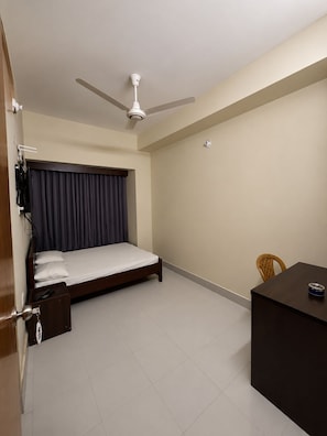 A bedroom with a bed, a ceiling fan, a desk, and a chair. - Hotel Al Barakah (Sylhet)