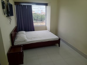 A bedroom with a single bed, a window with curtains, a wall-mounted telephone, and a small wooden cabinet. - Hotel Al Barakah (Sylhet)