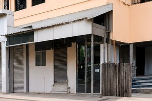 Um edifício com entrada coberta, persianas fechadas e escadaria que leva a um andar superior.