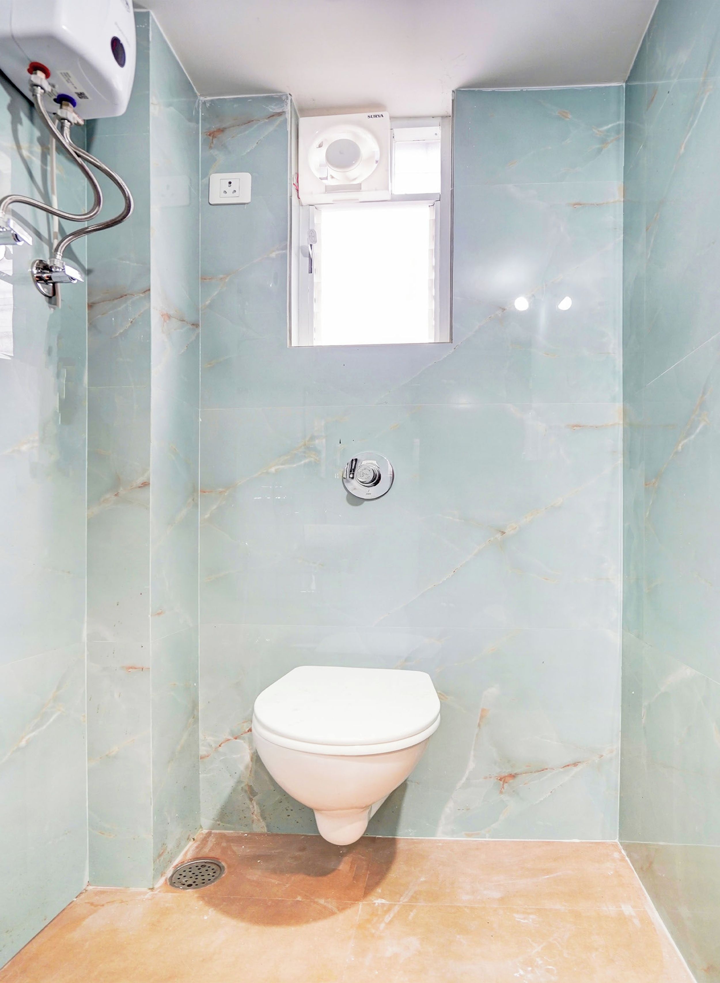 Un baño con inodoro, cabezal de ducha y una ventana pequeña.