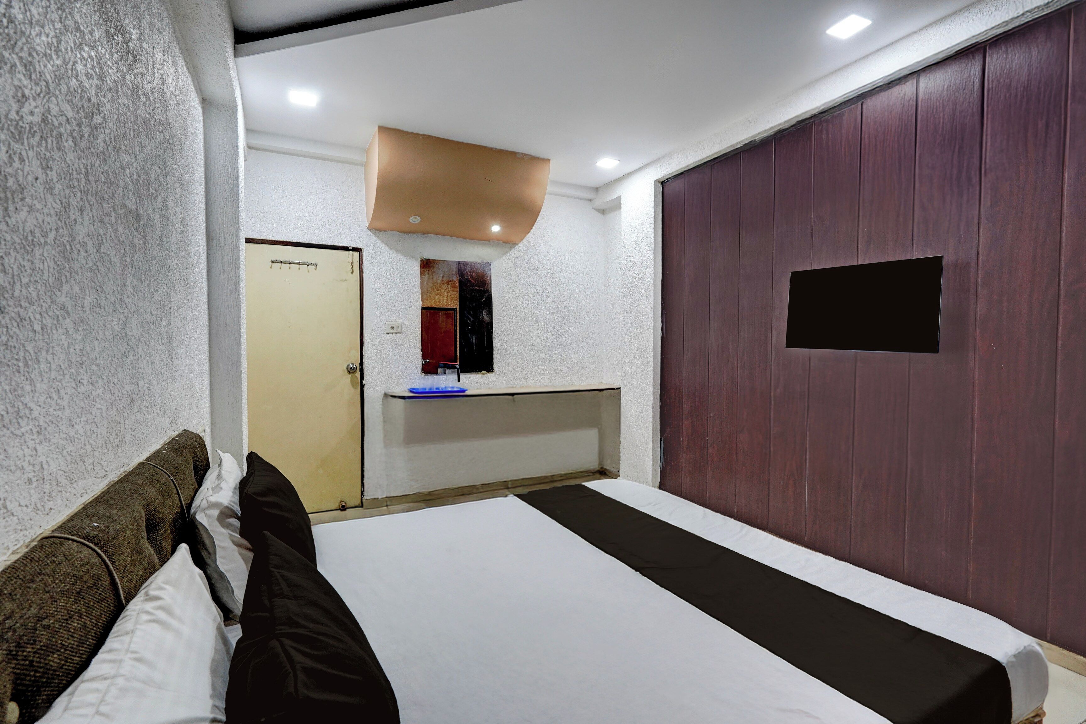 A hotel room with a bed, a small desk, a mirror, and a wardrobe.