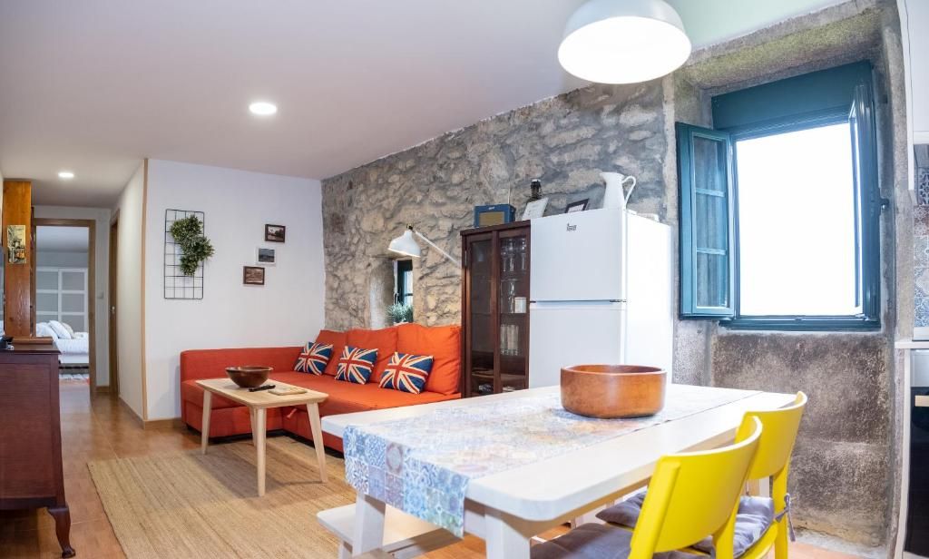 Ein Wohnzimmer mit einer Couch, einem Tisch und Stühlen, eine Küchenzeile mit Kühlschrank und eine Wand aus Stein.