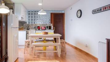 Een keuken met een houten tafel, witte kasten en een raam met glas-in-lood.