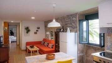 Un espacio habitable compacto con zona de comedor, un sofá con cojines, una cocina con estufa y una ventana con vistas.
