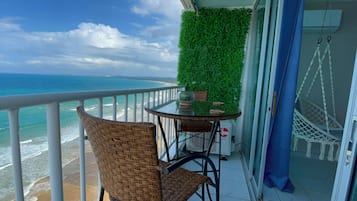 A balcony with a view of the ocean, a table with chairs, and a hanging chair.