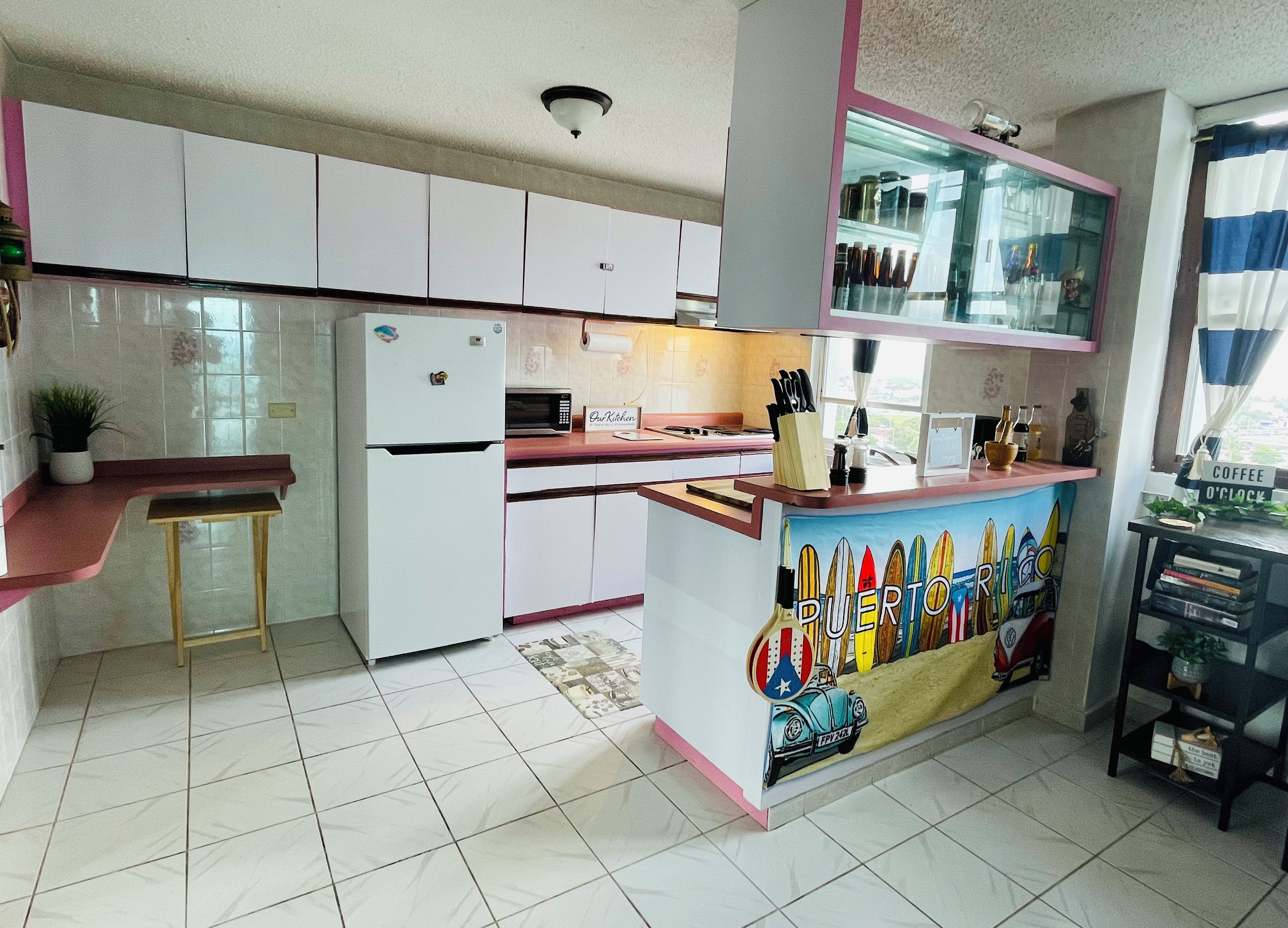 A kitchen with white cabinets, a refrigerator, a microwave, and a coffee station.