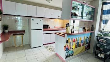 A kitchen with white cabinets, a refrigerator, a microwave, and a coffee station.
