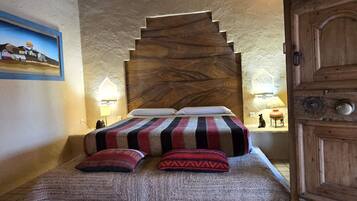 Una cama con colcha a rayas y dos almohadas, cabecera de madera y un cuadro en la pared.