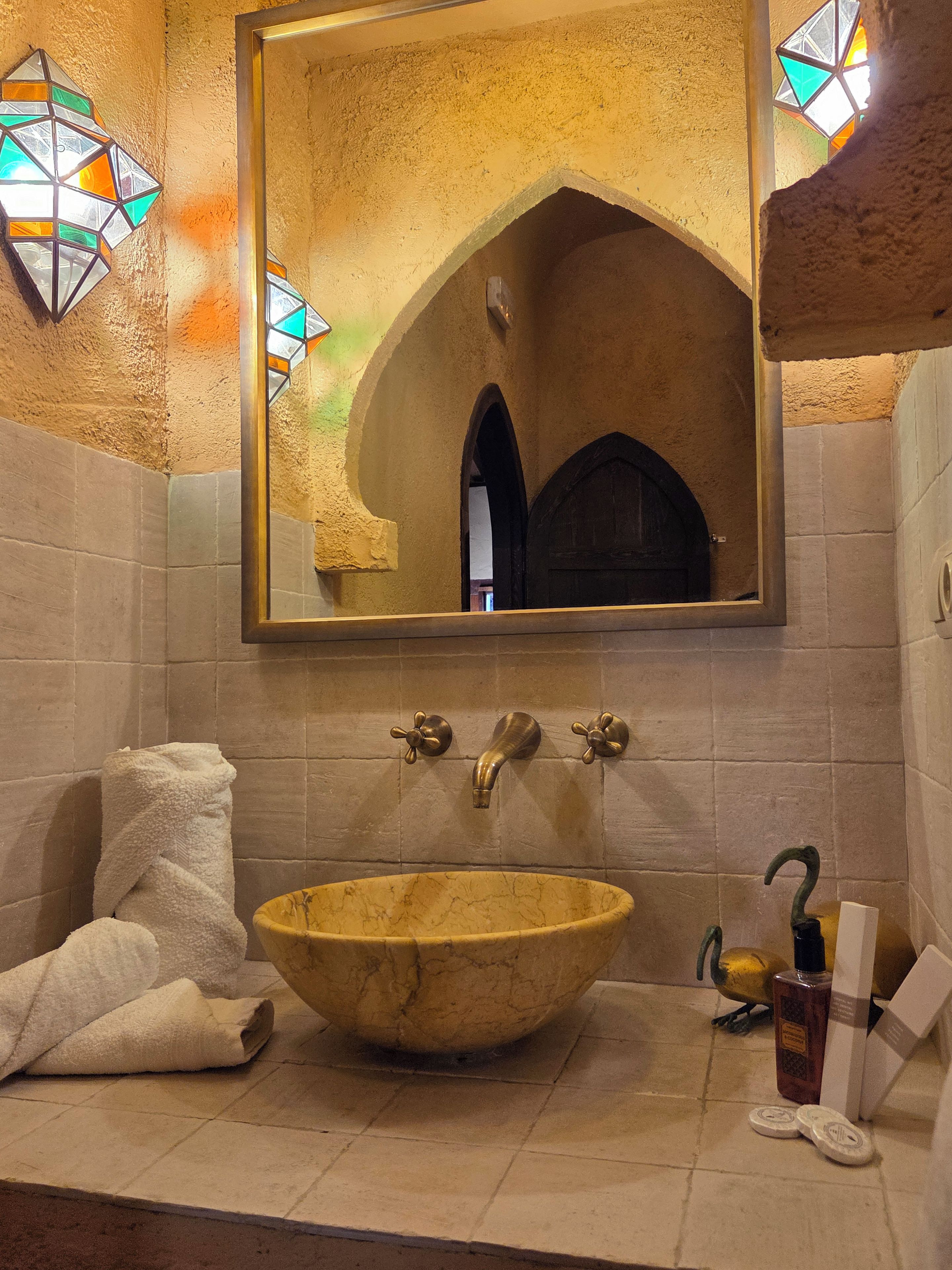 Une salle de bain avec un grand miroir, un lavabo en pierre et un porte-serviettes.