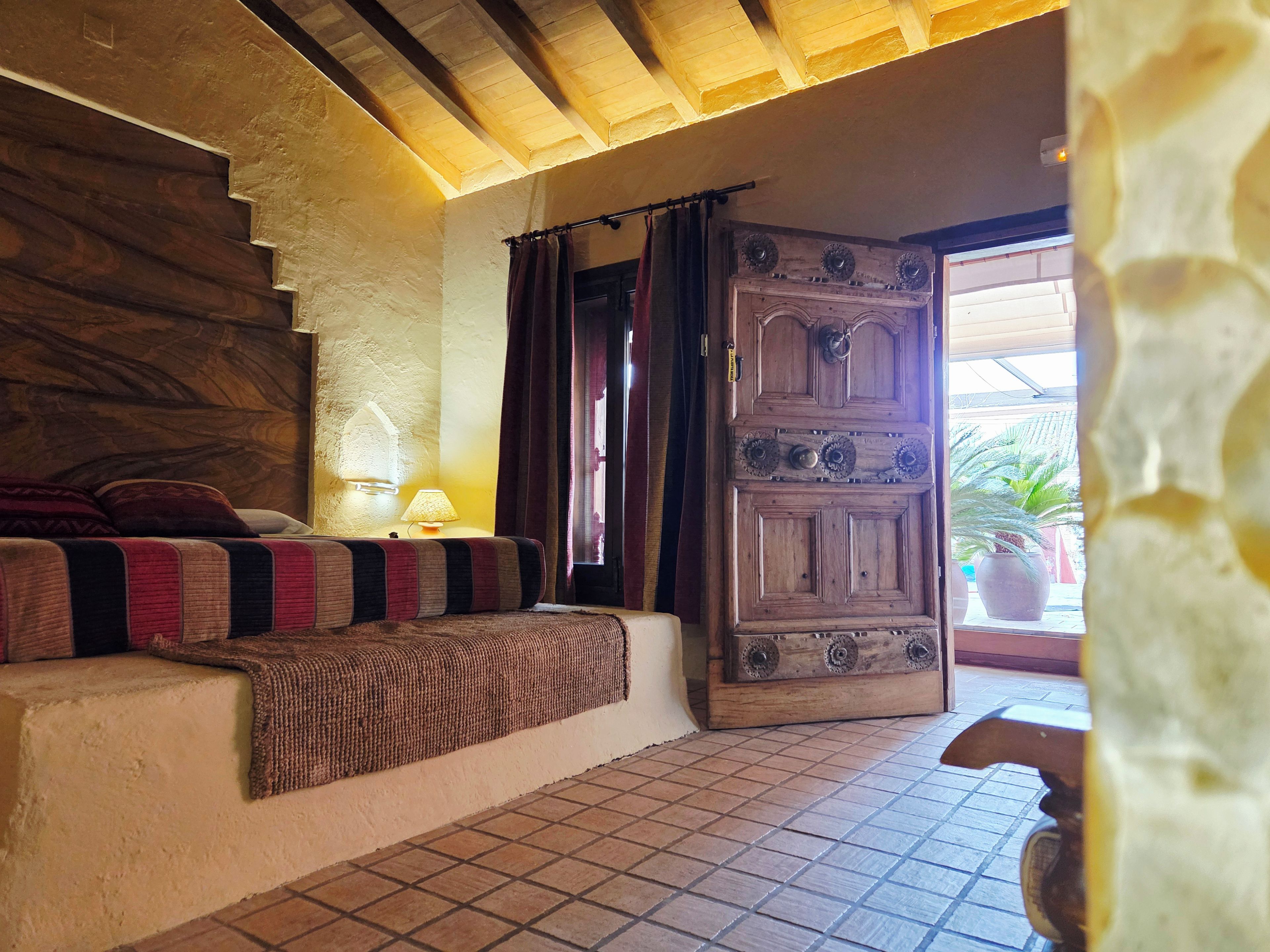 Una habitación con una escalera de madera, una cama con una colcha a rayas, una puerta de madera y un suelo de baldosas.
