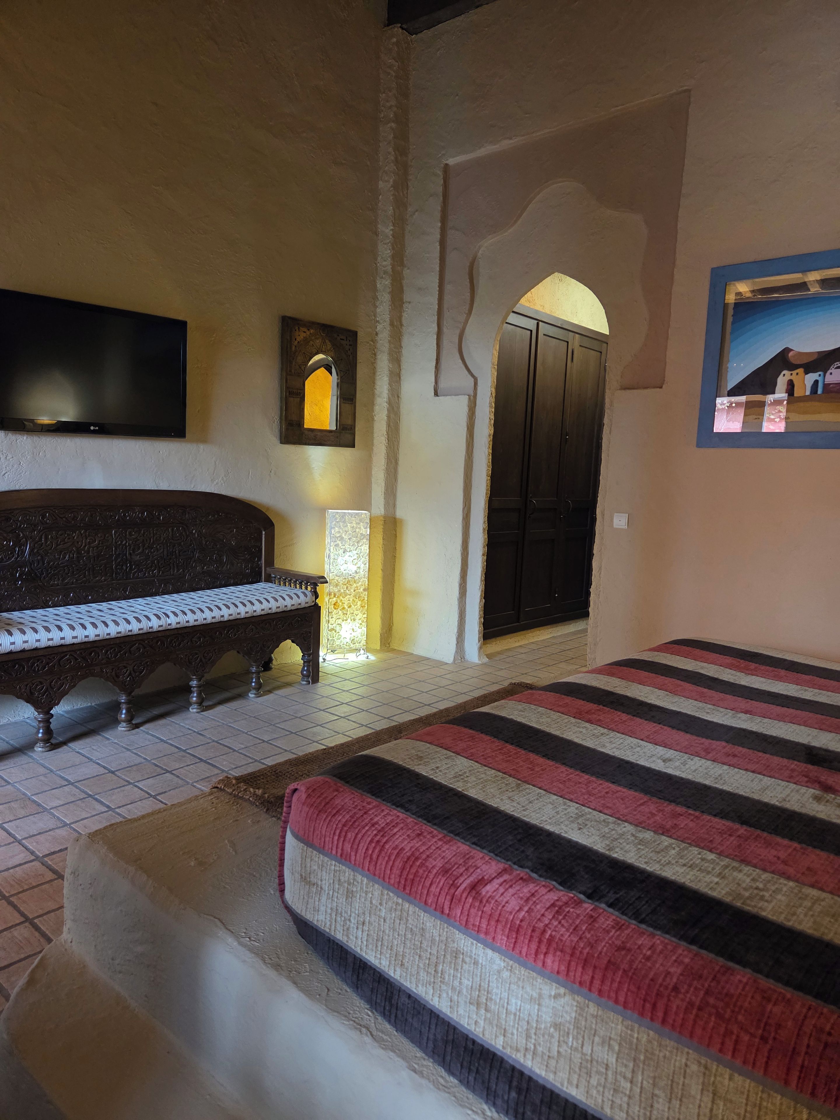 A room with a large bed, a bench, a television, and a door with an archway.