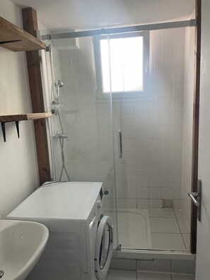 Un baño con cabina de ducha de vidrio, lavadora y lavamanos.
