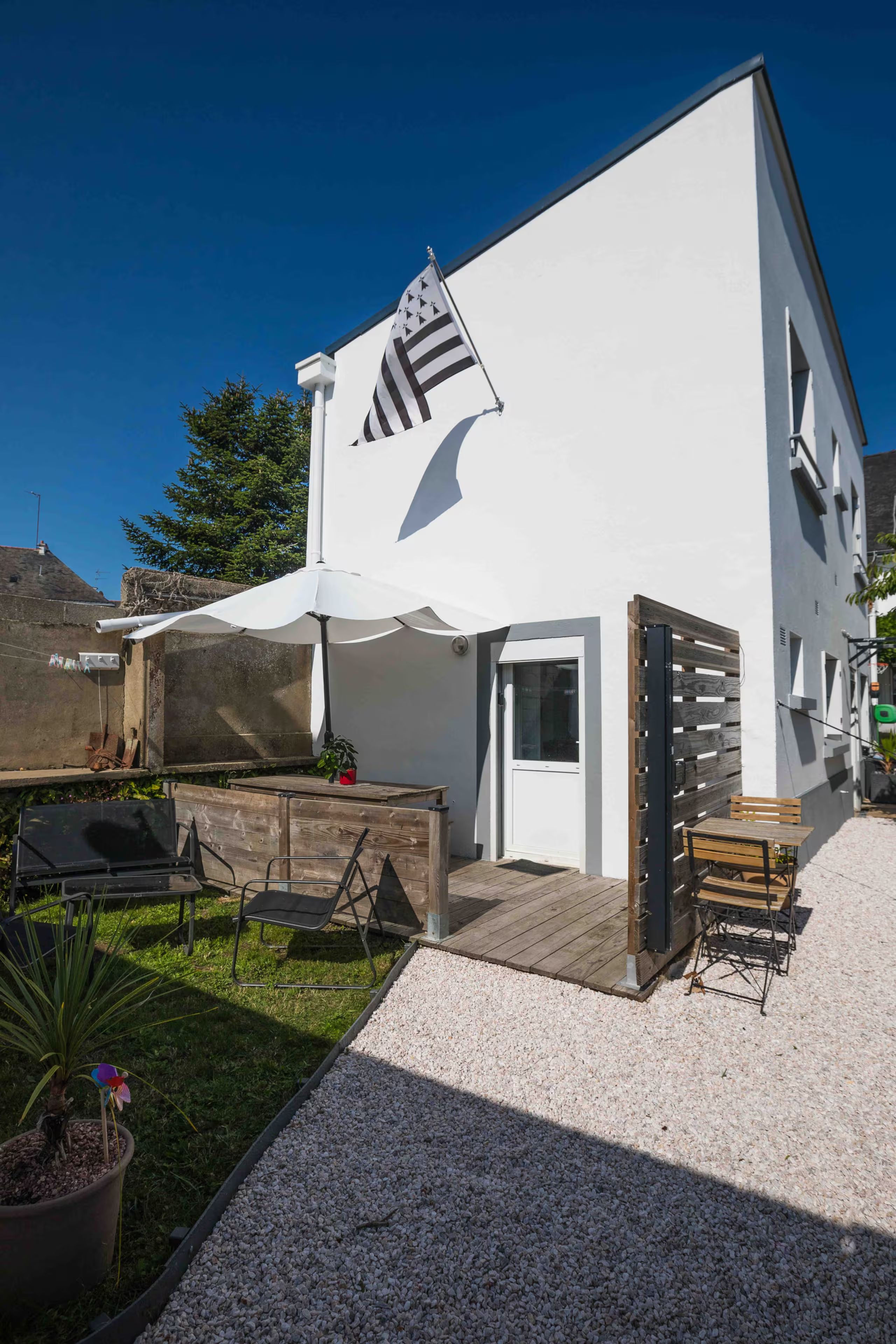 Een modern, tweelaags huis met een witte gevel, een balkon met een witte luifel en een houten terras.