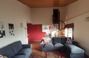 A modern living room with a red accent wall, a staircase, and a view of the dining area.