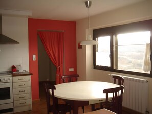 A dining area with a round table, chairs, a window with curtains, a stove, and a red wall.