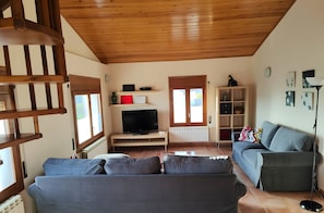 A living room with a wooden ceiling, a television on a stand, a sofa, a cabinet, and a floor lamp.