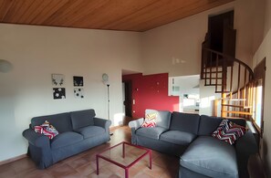 Un salon avec deux canapés gris, une table basse rouge et un escalier menant à un niveau supérieur.