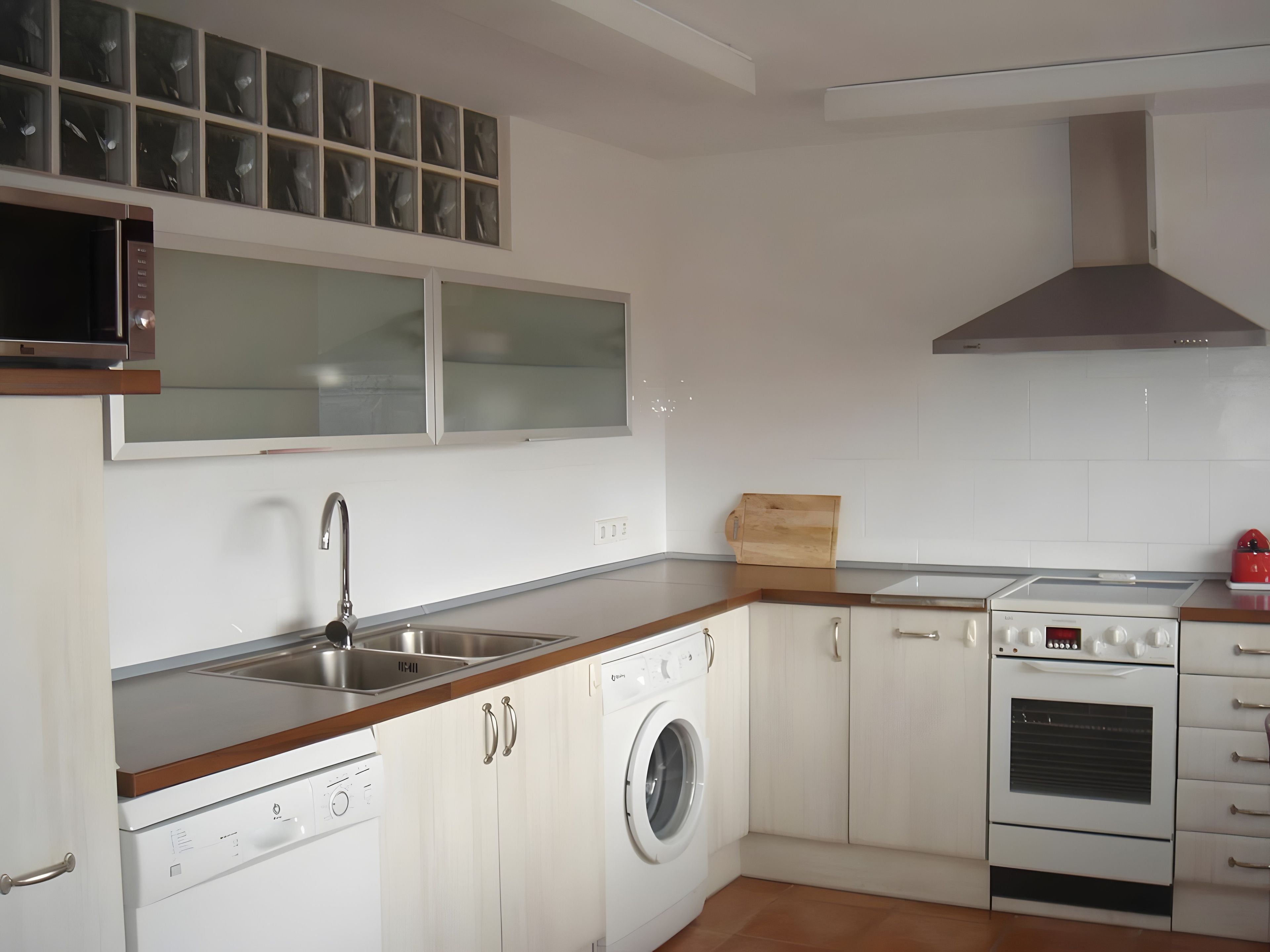 Una cocina moderna con lavavajillas integrado, pileta de acero inoxidable, microondas, estufa y un ventanal sobre la pileta.