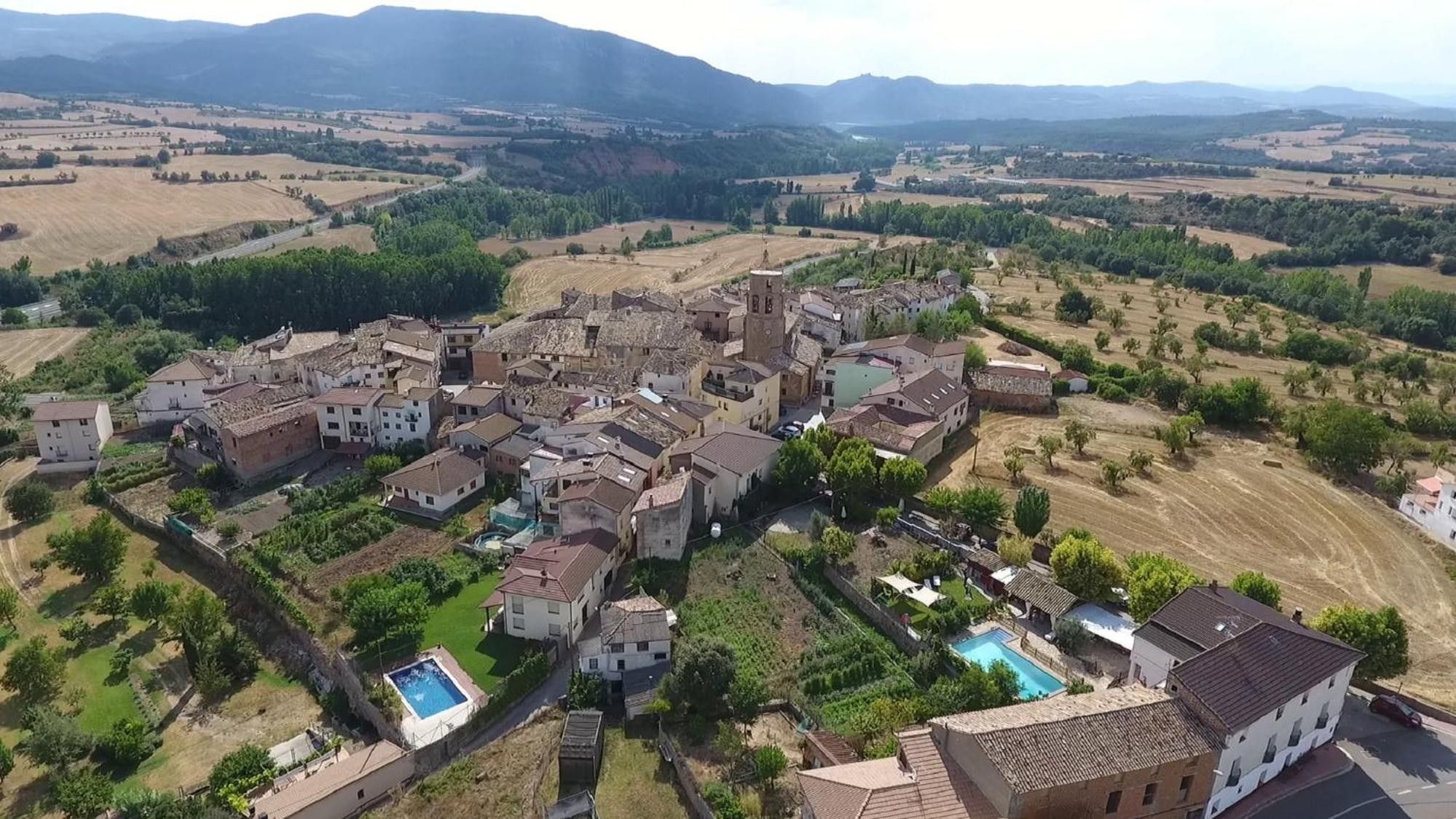 Un village aux bâtiments regroupés, doté d’une piscine et entouré de champs agricoles.