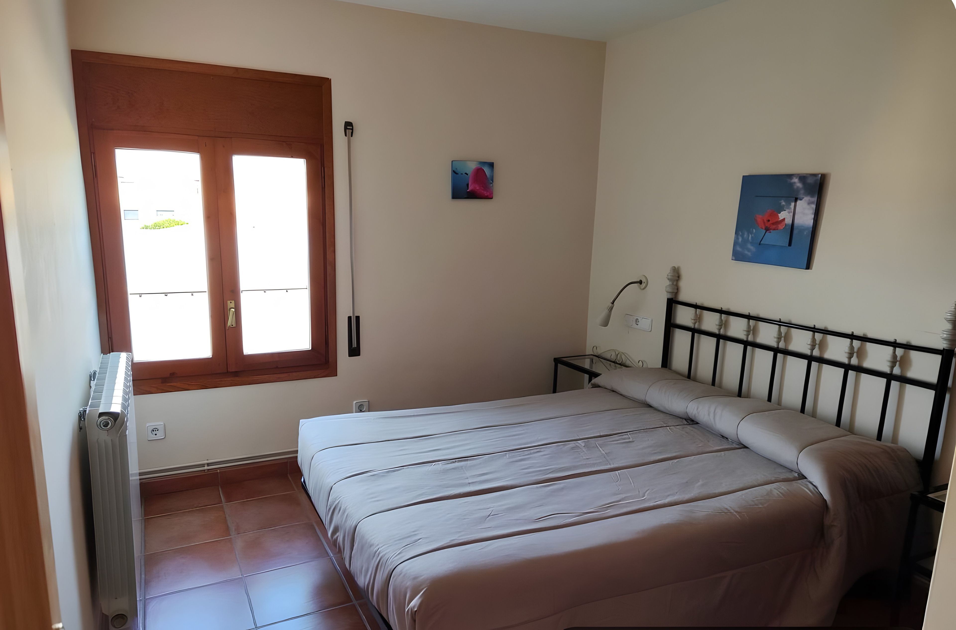 Un dormitorio con cama, radiador, ventana y lámpara fijada en la pared.
