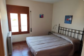 A bedroom with a bed, a radiator, a window, and a wall-mounted lamp.