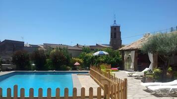 Una piscina azul cristalina con una cerca de madera, una torre del reloj y un letrero que dice 'TORRES DEL OBISPO' al fondo.