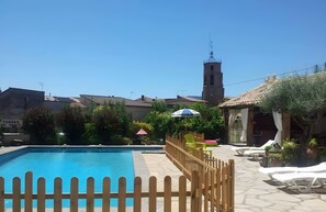 A clear blue swimming pool with a wooden fence, a clock tower, and a sign reading 'TORRES DEL OBISPO' in the background.