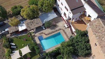 Eine Vogelperspektive auf ein Wohnhaus mit Swimmingpool, Gartenmöbeln und einem weißen Gebäude mit mehreren Fenstern.