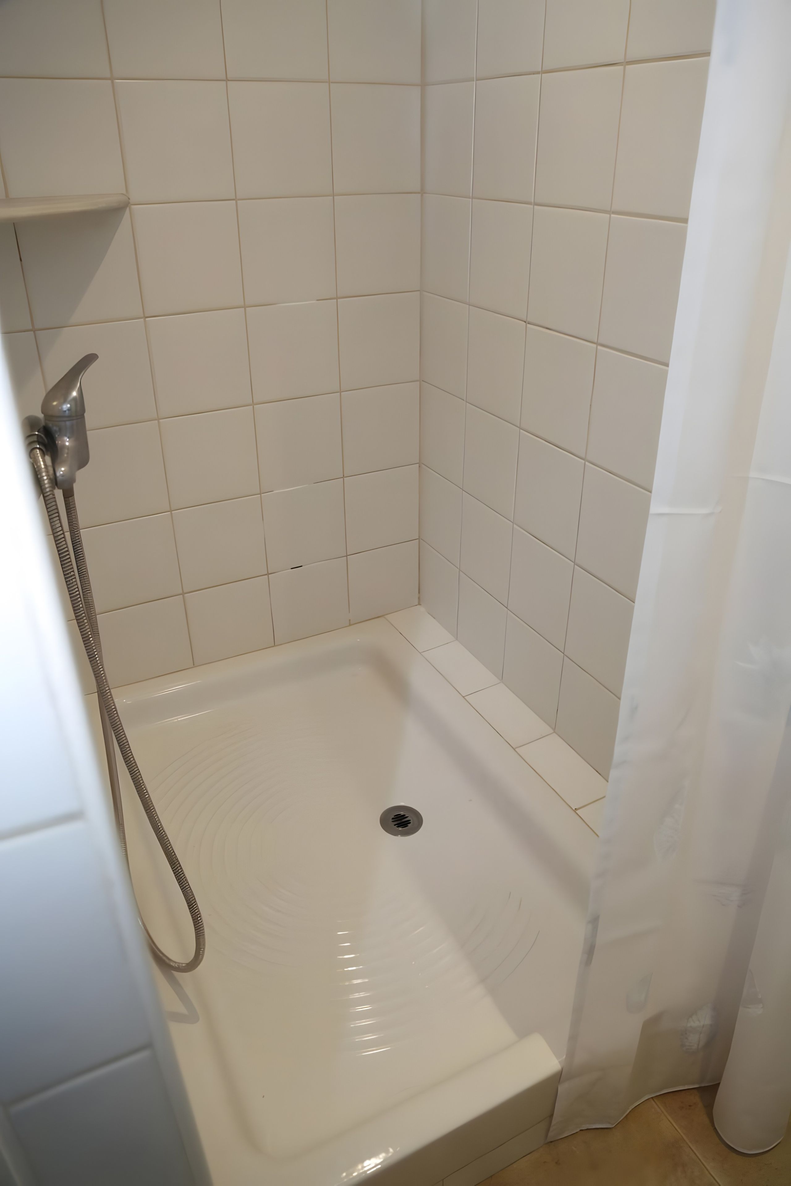 Ducha con azulejos blancos, cabezal de ducha y desagüe.