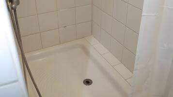 Ducha con azulejos blancos, cabezal de ducha y desagüe.