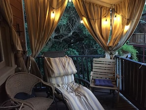 A balcony with a wicker chair, a cushioned bench, and a striped bed.