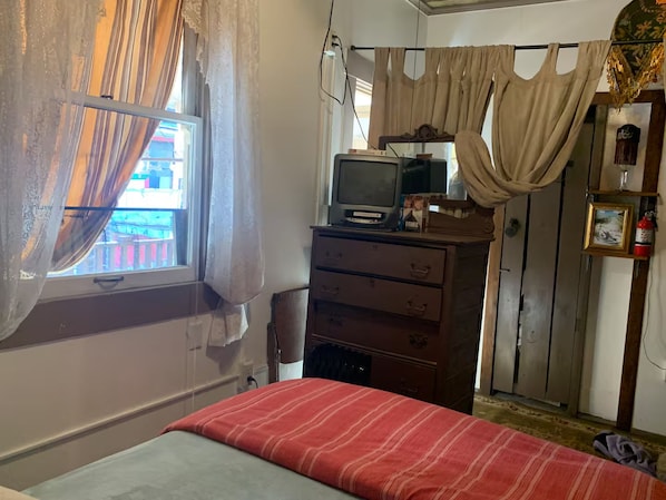 A room with a bed, a dresser, a television on top, and a window with curtains.