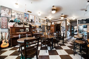 Un restaurante con piso a cuadros, mesas y sillas de madera, y varias fotografías enmarcadas en las paredes.