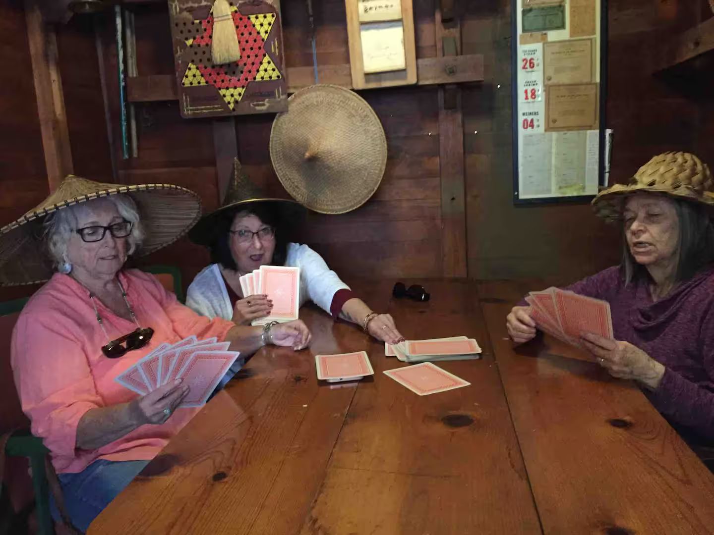 Three individuals seated at a wooden table playing cards.