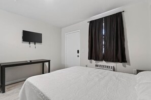 A bedroom with a bed, a desk, a television, and a door.