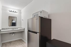 Een kleine keuken met een roestvrijstalen koelkast, een magnetron, een spoelbak met een granieten aanrecht en een spiegel boven de spoelbak.