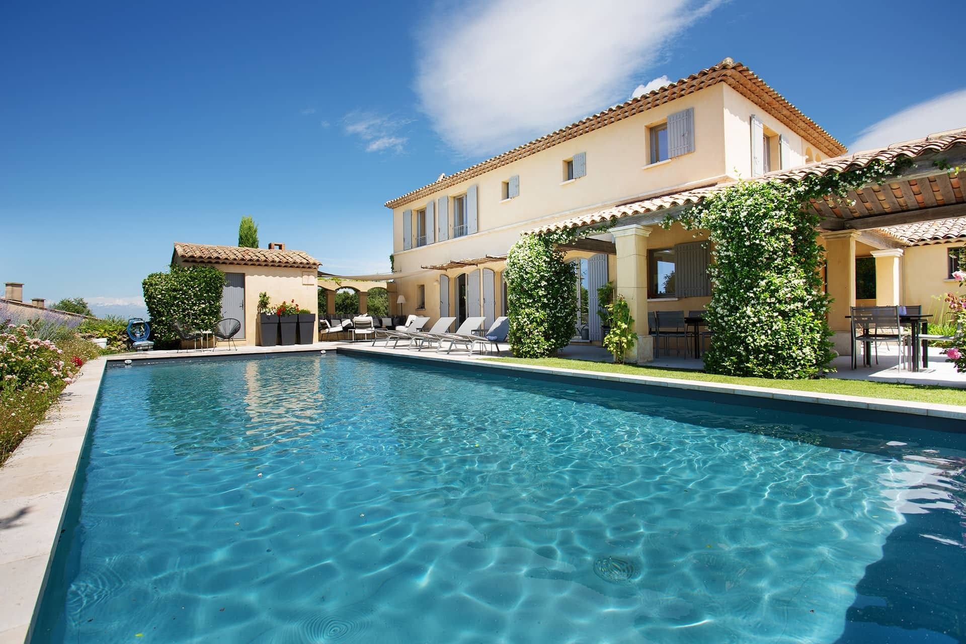 A swimming pool with lounge chairs and a building with a tiled roof.