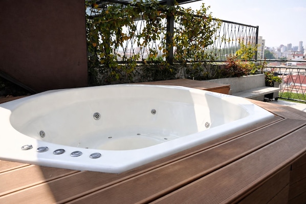 Un jacuzzi en una terraza de madera con vista a la ciudad al fondo.