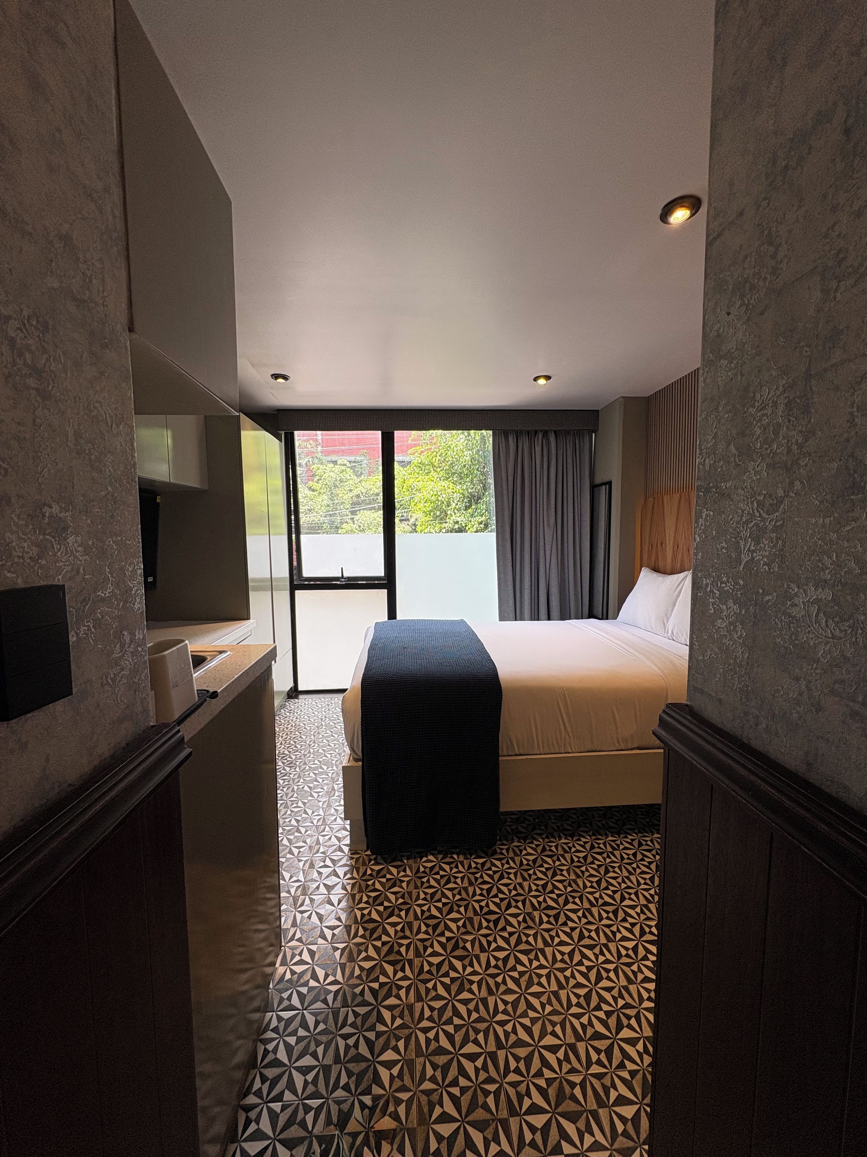 Habitación de hotel con cama, escritorio, televisor y vistas al exterior.
