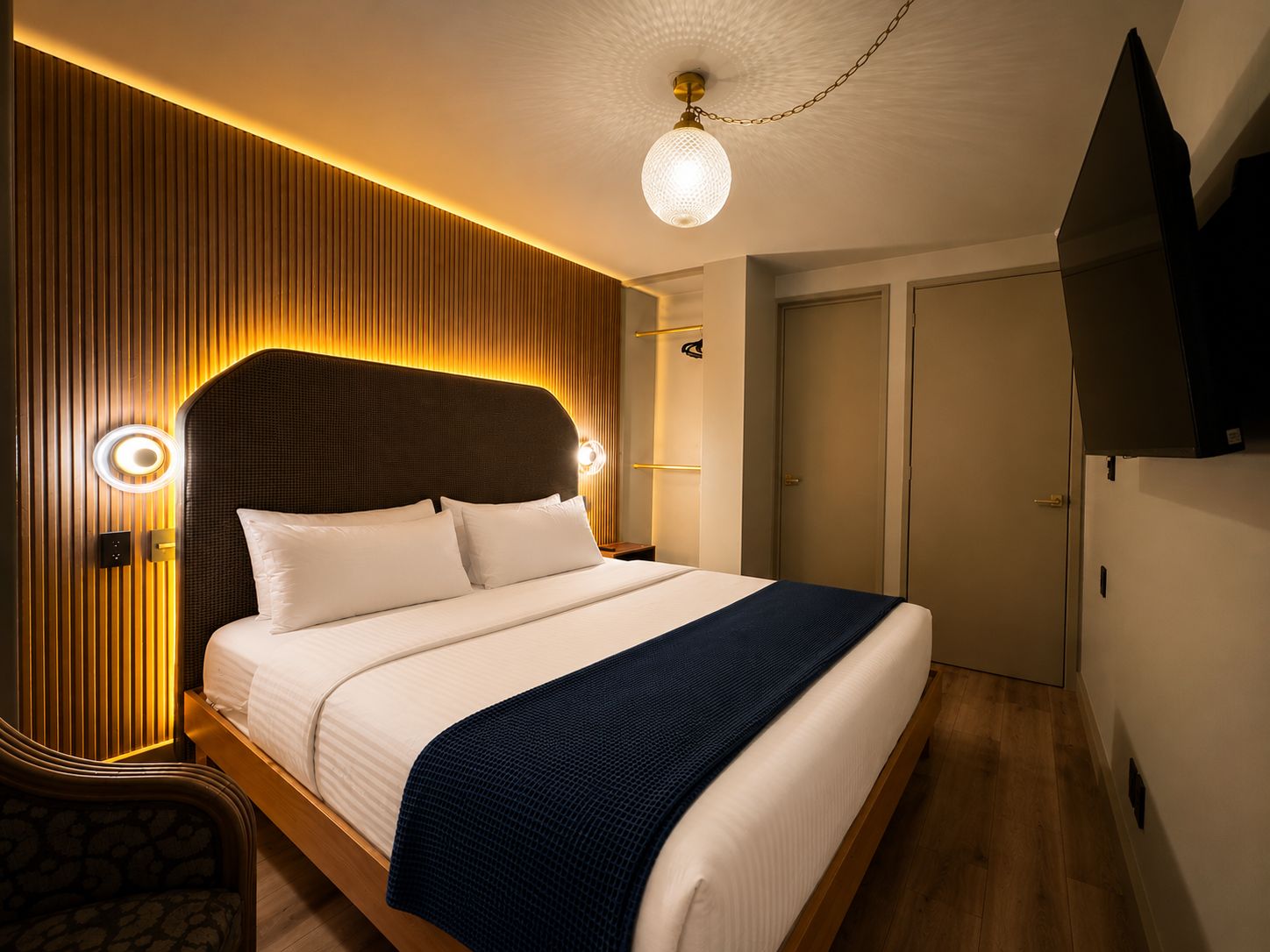 Una habitación de hotel moderna con una cama grande, paneles de madera y un televisor de pantalla plana montado en la pared.