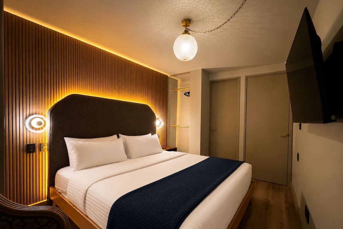 Una habitación de hotel moderna con una cama grande, paneles de madera y un televisor de pantalla plana montado en la pared.
