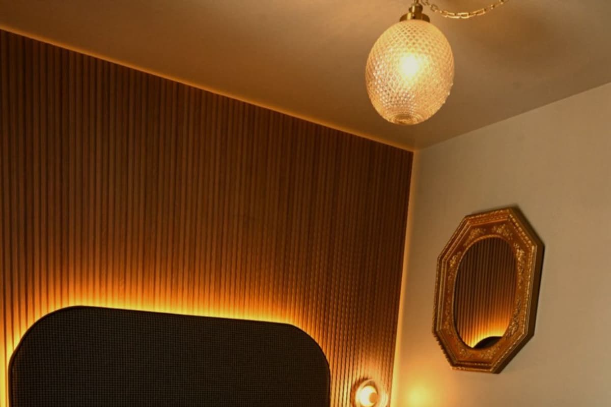 Una cama bien hecha con cabecera, una mesita de noche con lámpara y un adorno en la pared.