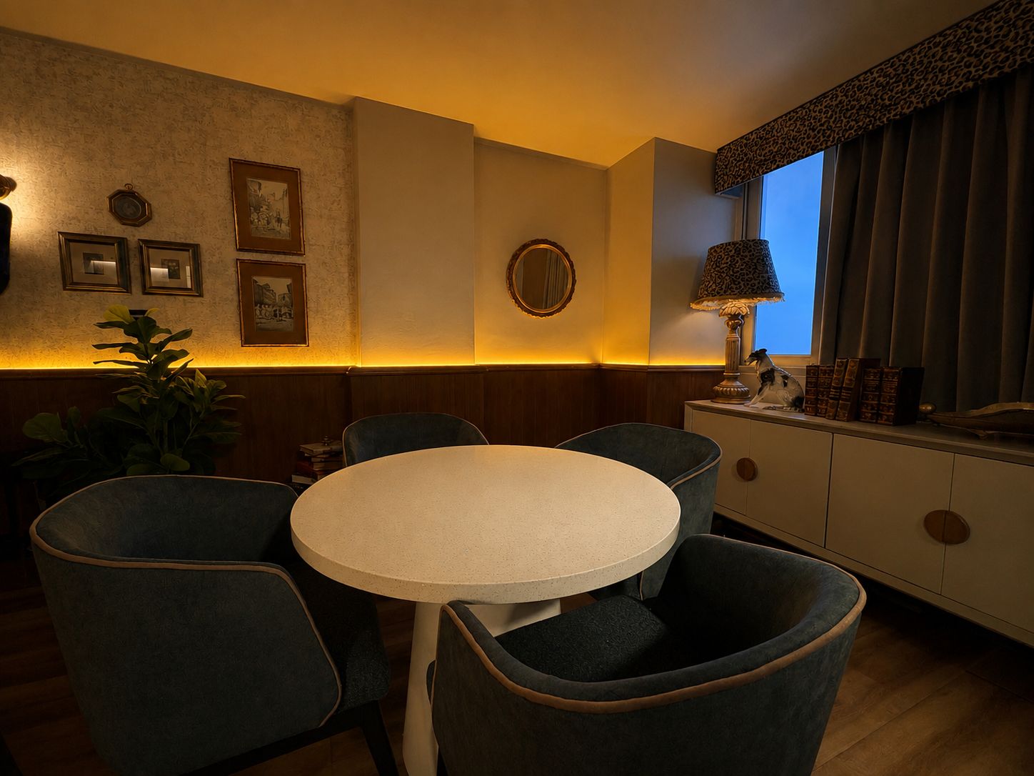 Un comedor con una mesa redonda y cuatro sillas, un espejo, cuadros enmarcados en la pared y una ventana con cortinas.