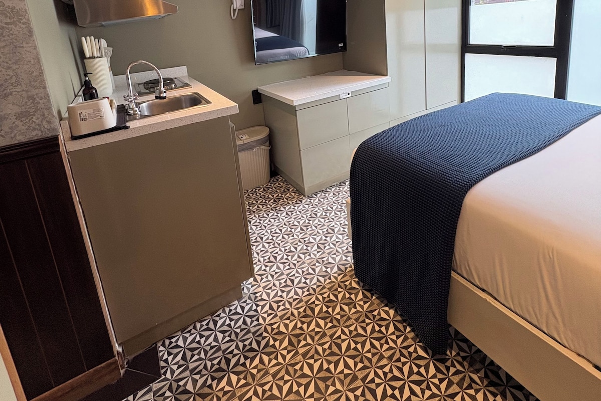 Habitación de hotel compacta con kitchenette, cama, televisor y ventana con vistas.